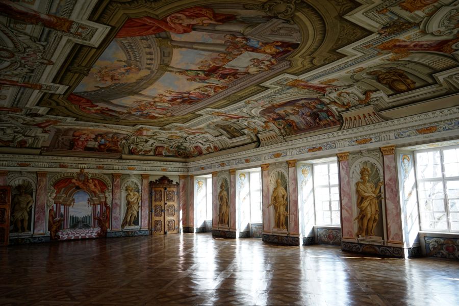 Innenansicht eines prächtig dekorierten Raumes mit einem kunstvoll gemaltem Deckenfresko und dekorativen Wänden, die Statuen und Malereien zeigen.