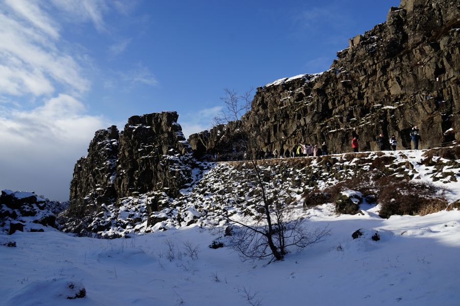 Schneebedeckte Felsen und eine Gruppe von Wanderern entlang eines schmalen Pfades unter einem blauen Himmel.