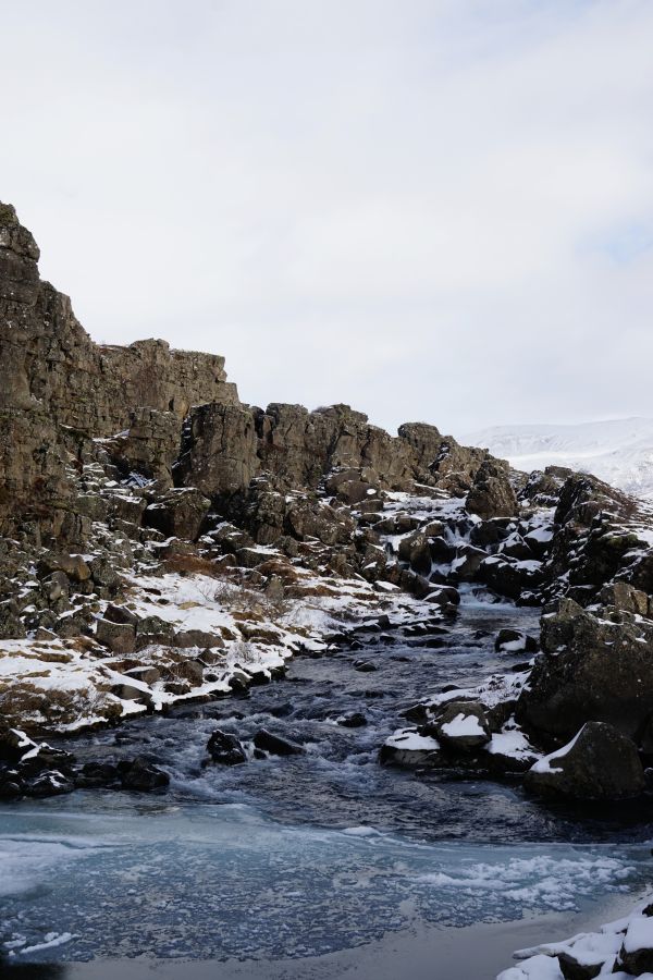 Eine Schneelandschaft mit einem kleinen Fluss, umgeben von schroffen Felsen und schneebedecktem Terrain.