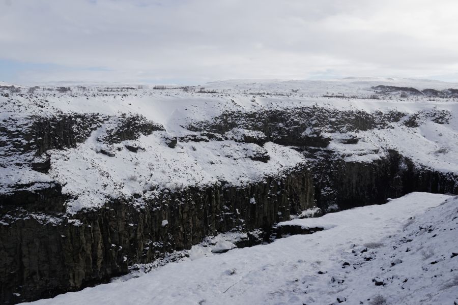 Schneebedeckte Landschaft mit steilen Klippen und schneebedecktem Boden in einem isländischen Nationalpark, unter einem bewölkten Himmel.