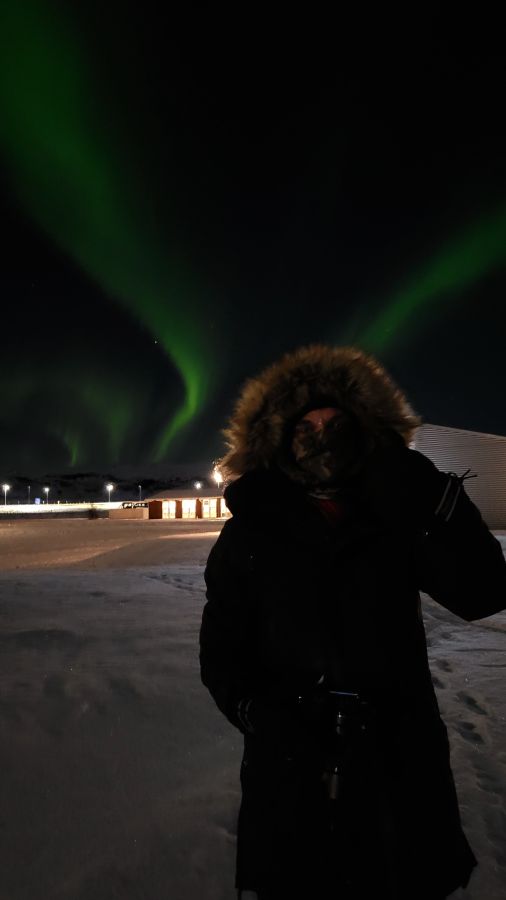 Eine Person steht im Vordergrund vor dem spektakulären Hintergrund der Nordlichter, die in lebendigen grünen Farben am Nachthimmel tanzen.