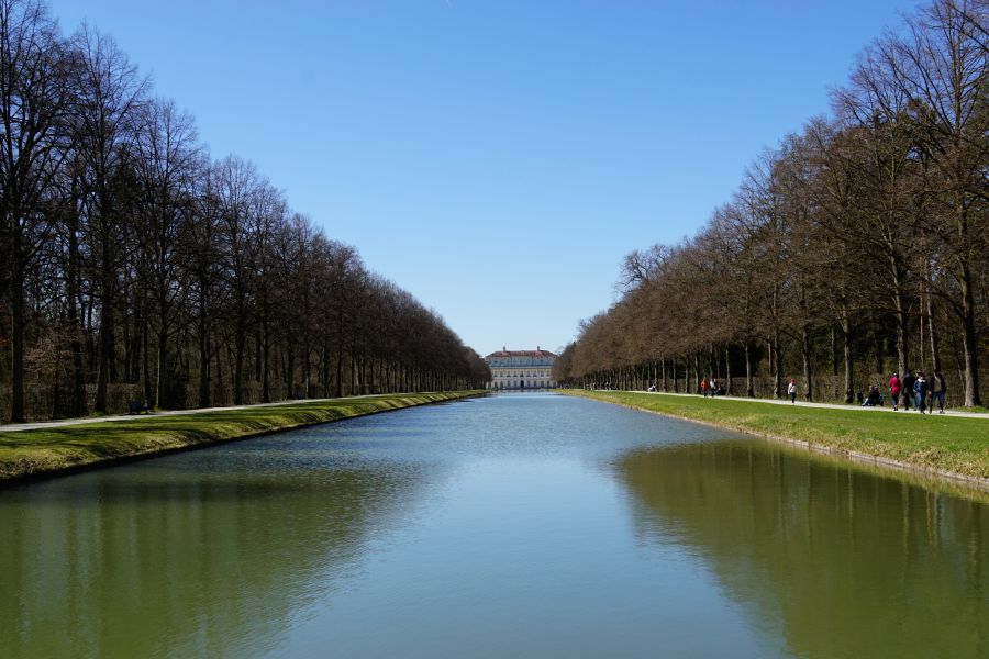Blick auf die barocke Schlossanlage Schleißheim mit Wasserkanal und umstehenden Bäumen an einem klaren Tag.