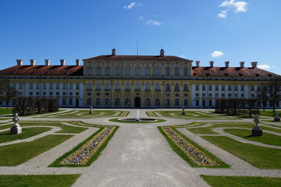 Die barocke Wittelsbacher Sommerresidenz Schlossanlage Schleißheim mit gepflegtem Garten und Blumenrabatten unter blauem Himmel.