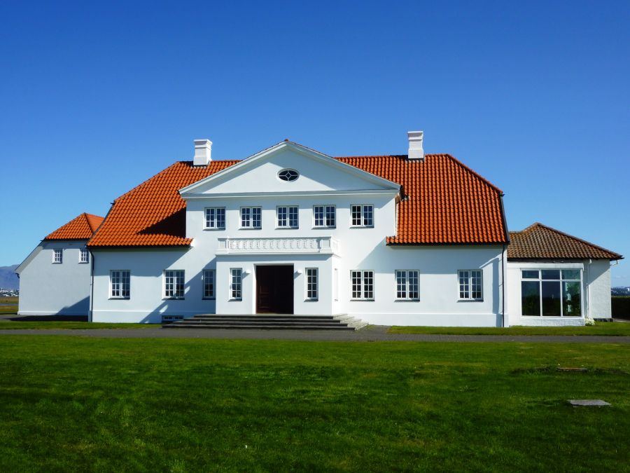 Ein großes, weißes Gebäude mit rotem Dach und klar blauem Himmel im Hintergrund, umgeben von großzügigen grünen Flächen.