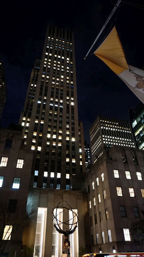 Nachtaufnahme des Rockefeller Centers in New York mit beleuchteten Wolkenkratzern und der Statue des Atlas im Vordergrund.