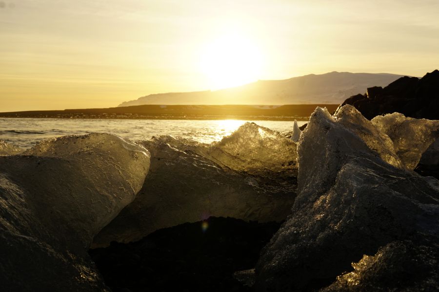 Sonnenuntergang über einem Gletschersee, mit Eisblöcken im Vordergrund und einer goldenen Himmelstönung.