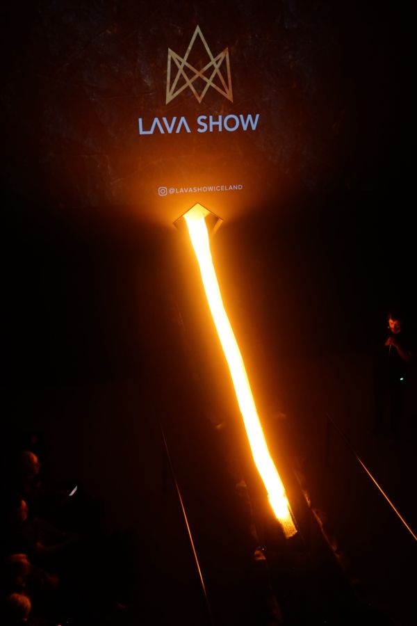 Eine Darstellung der Lava Show in Island, bei der flüssige Lava aus einer künstlichen Quelle fließt, während ein Logo mit der Aufschrift 'LAVA SHOW' im Hintergrund leuchtet.