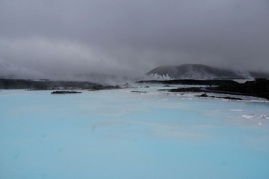 Blick auf die Blaue Lagune in Island, umgeben von dampfenden geothermalen Quellen und grauem Himmel.