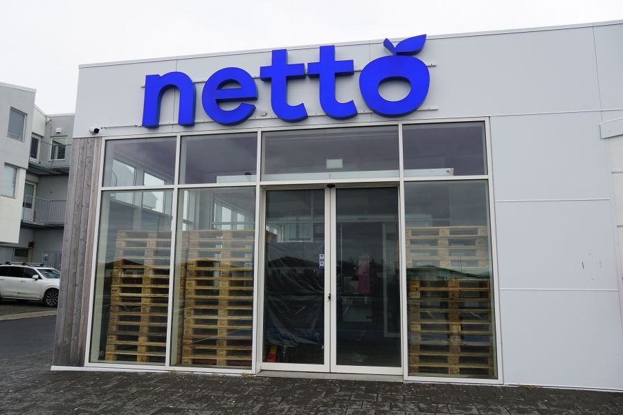 Eingang zu einem Netto-Supermarkt mit blauer Schrift und leeren Holzpaletten im Fenster.