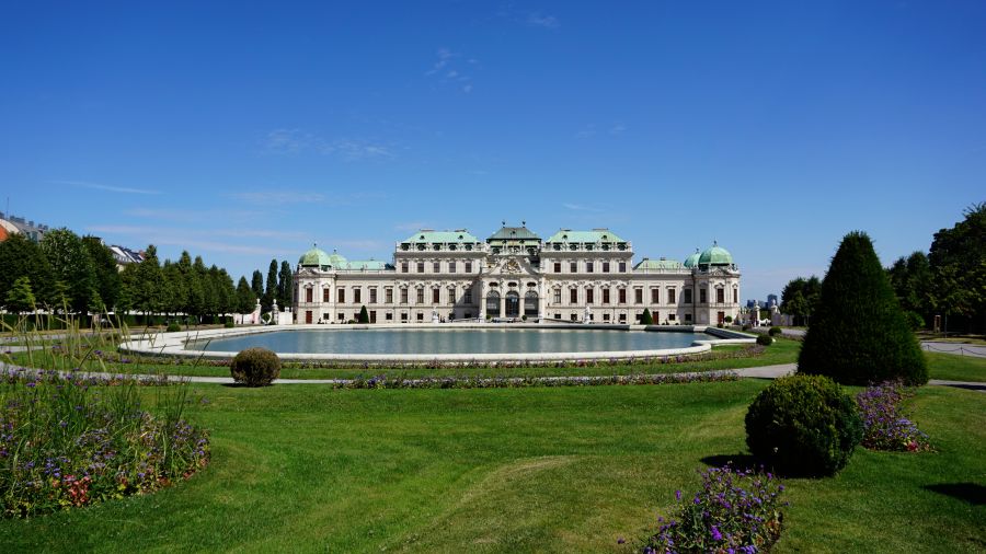 Das Schloss Belvedere in Wien, umgeben von gepflegten Grünflächen und Blumenbeeten, unter einem klaren blauen Himmel.