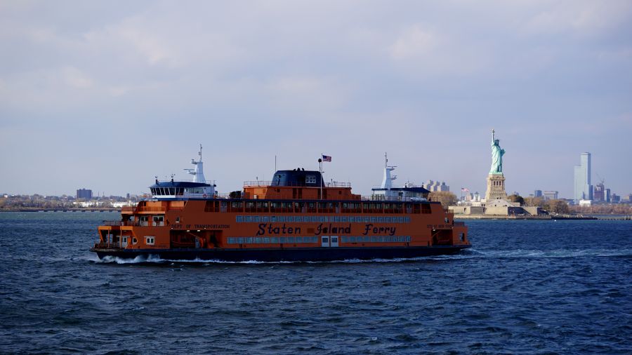 Ein oranger Staten Island Ferry-Boot fährt im Wasser mit der Freiheitsstatue im Hintergrund.