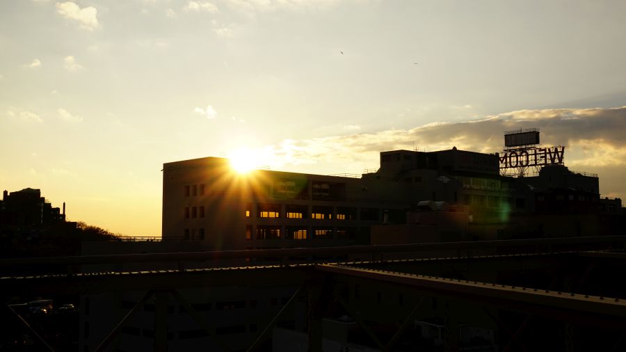 Sonnenuntergang über New York City, mit Gebäuden im Vordergrund silhouettiert und der Sonne, die zwischen ihnen aufgeht.