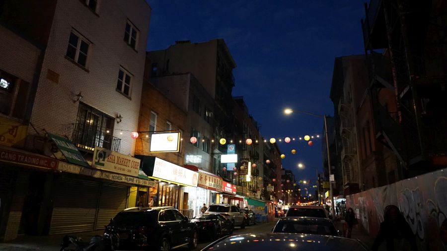 Beleuchtete Straße in Chinatown mit Geschäften und bunten Laternen bei Nacht.