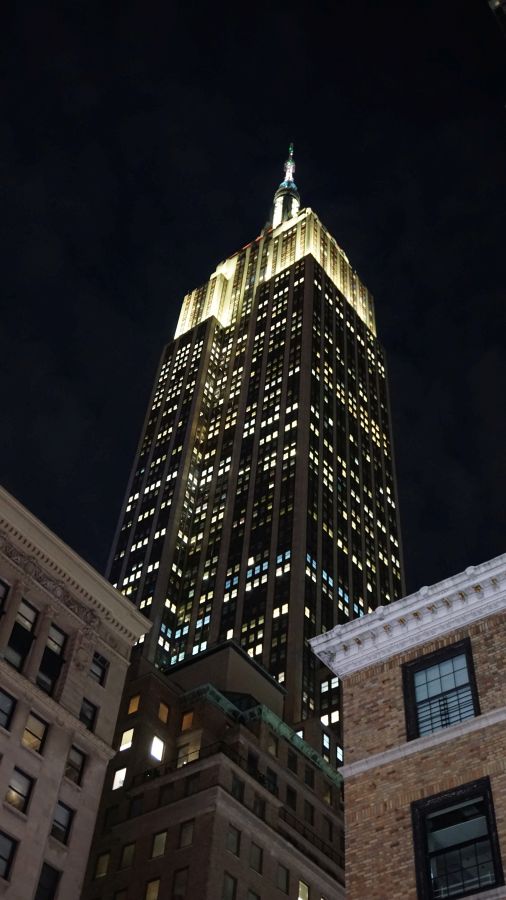 Das Empire State Building erstrahlt in der Nacht, umgeben von kleineren Gebäuden und einem klaren, dunklen Himmel.