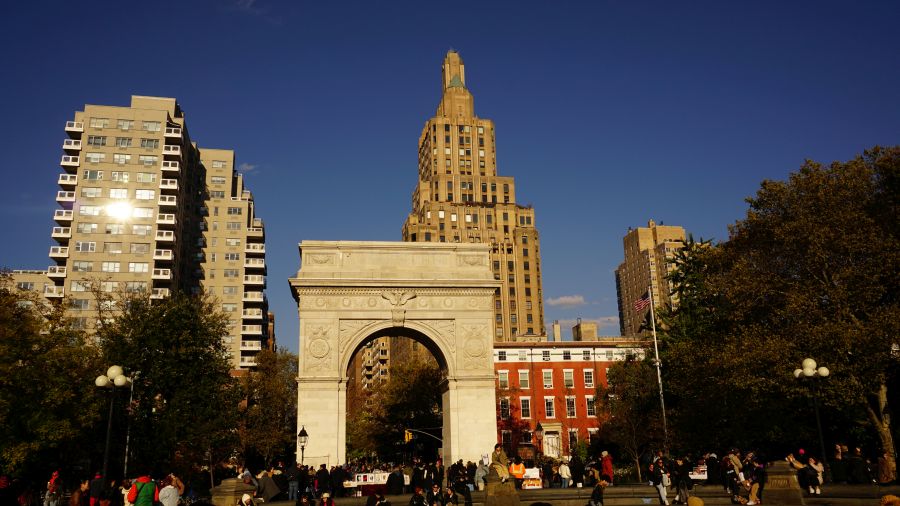 Der Washington Square Park mit dem ikonischen Triumphbogen und Hochhäusern im Hintergrund, bei sonnigem Wetter.