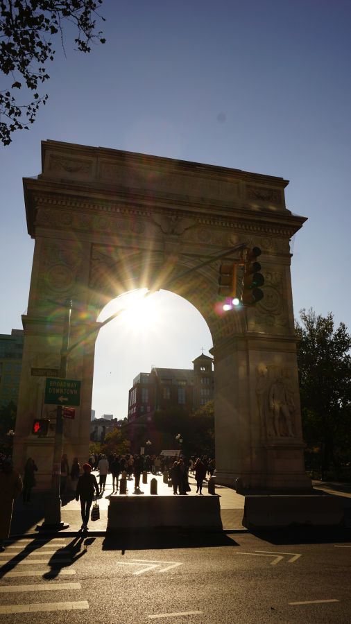 Sonnenuntergang hinter dem Washington Square Arch in New York, mit Fußgängern und Stadtgebäuden im Hintergrund.