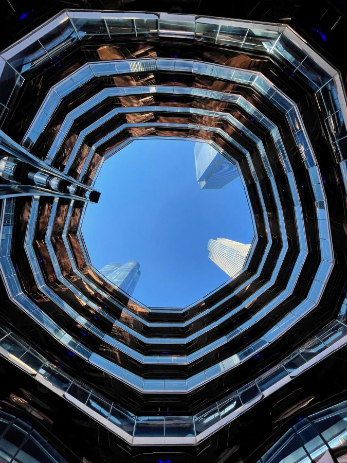Blick nach oben in die Architektur des Vessel im Hudson Yards mit einem klaren blauen Himmel im Hintergrund.
