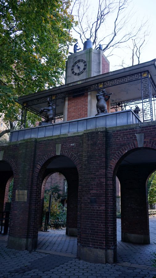 Eine skulpturale Uhr an einem historisch gestalteten Gebäude im Central Park, umgeben von Bäumen und grüner Vegetation.