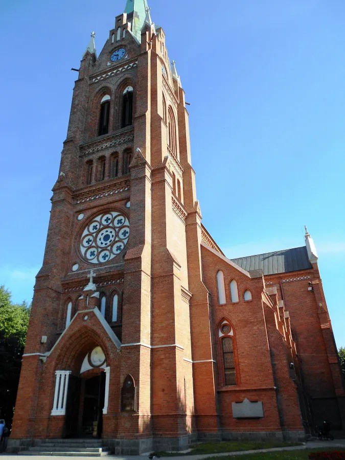 A tall brick church with a clock tower and ornamental windows against a clear blue sky.