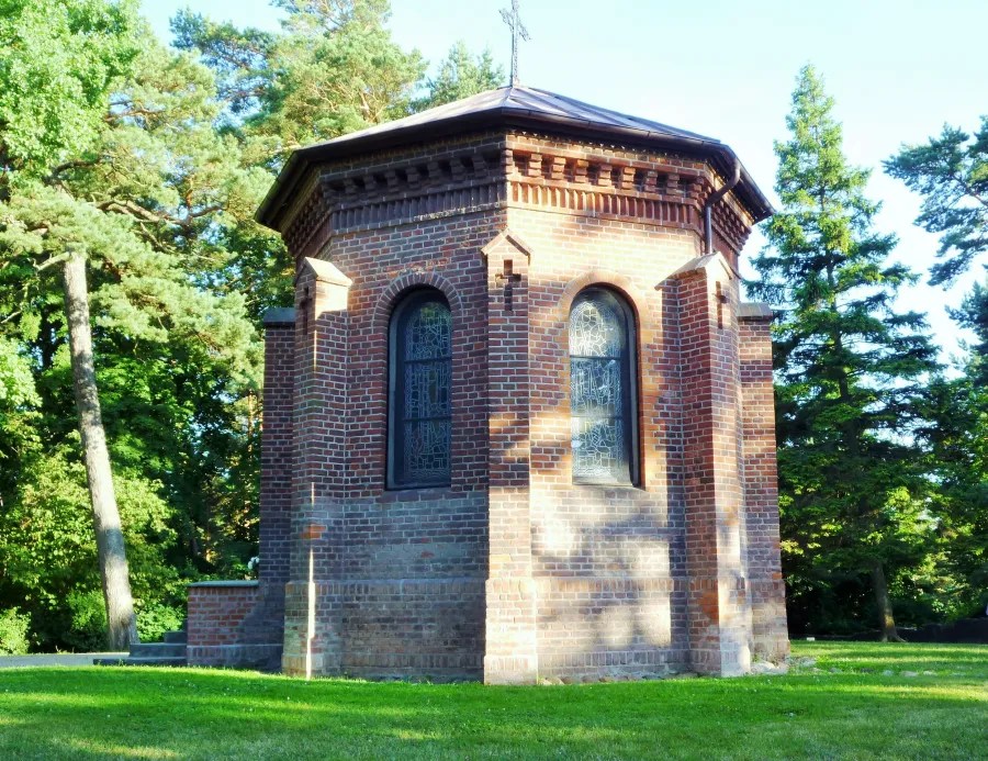 A small octagonal brick chapel surrounded by trees, featuring stained glass windows.