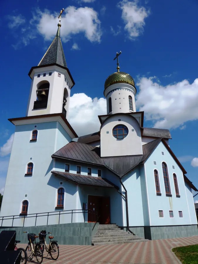 A blue and white church with a golden dome and a bell tower against a bright blue sky, featuring bicycles parked in front.