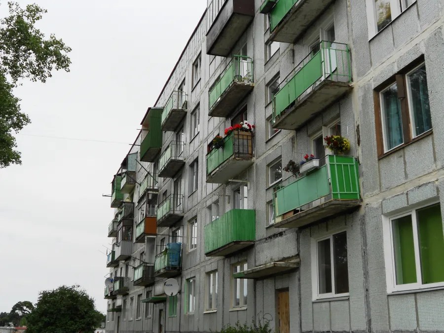 Ansicht eines mehrstöckigen Wohngebäudes mit grünen Balkonen und Fenstern, umgeben von Bäumen.