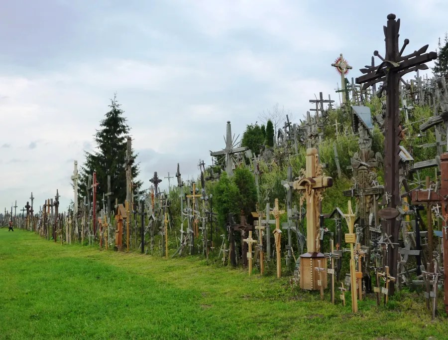 Berg der Kreuze in Siauliai mit zahlreichen Holz- und Metallkreuzen, umgeben von Gras und Bäumen unter einem bewölkten Himmel.