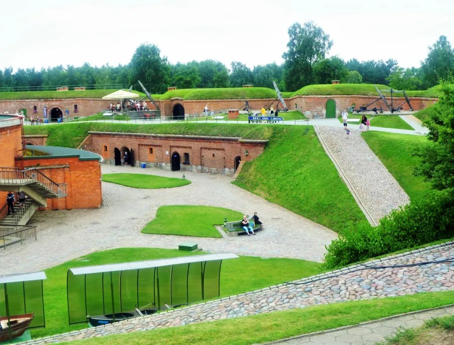 Ein historischer Fort-Komplex mit grünen Wiesen, gepflasterten Wegen und Besuchern, die sich im Freien aufhalten.