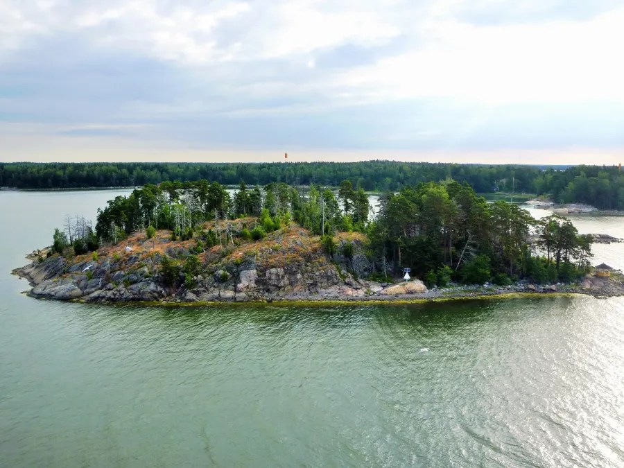 Aerial view of a rocky island with lush greenery surrounded by calm waters under a cloudy sky.
