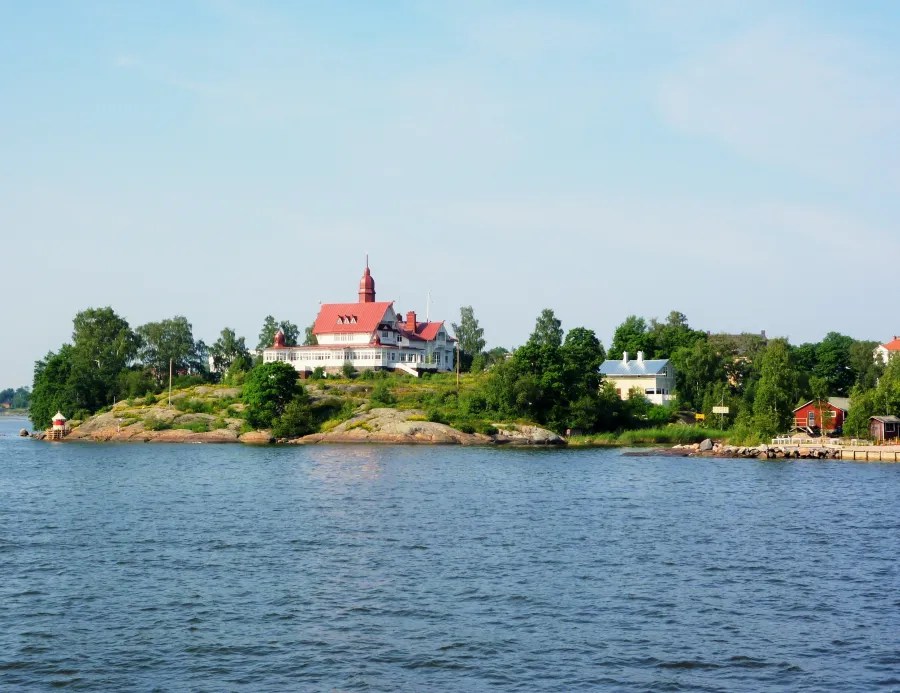 View of a coastal landscape with a historic building on an island, surrounded by greenery and water.