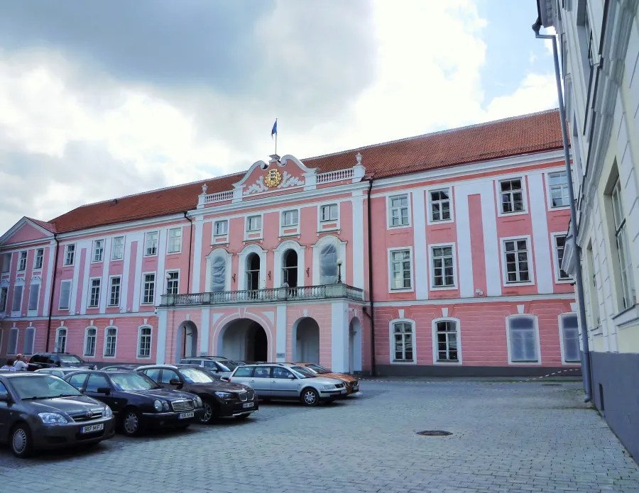 Exterior view of a pink historical building with a balcony and a flag, surrounded by parked cars.