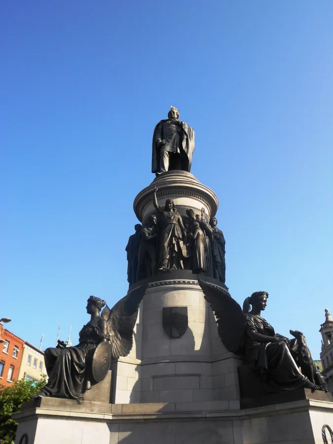 Eine monumentale Statue mit Skulpturen an der Basis vor klarem blauen Himmel in Dublin.