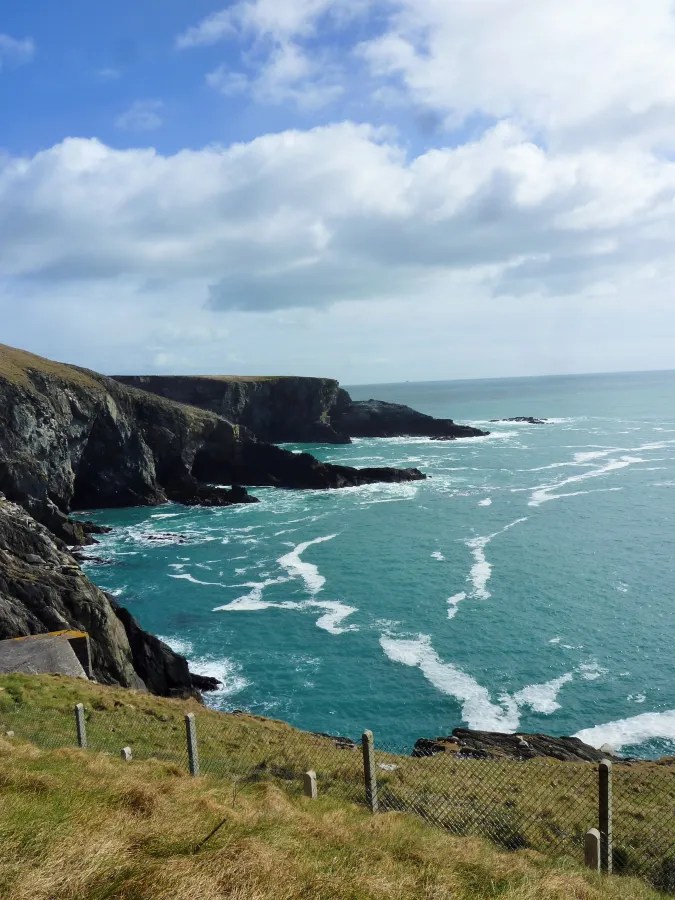 Eine beeindruckende Küstenlandschaft mit steilen Klippen und türkisfarbenem Wasser, unter einem bewölkten Himmel.