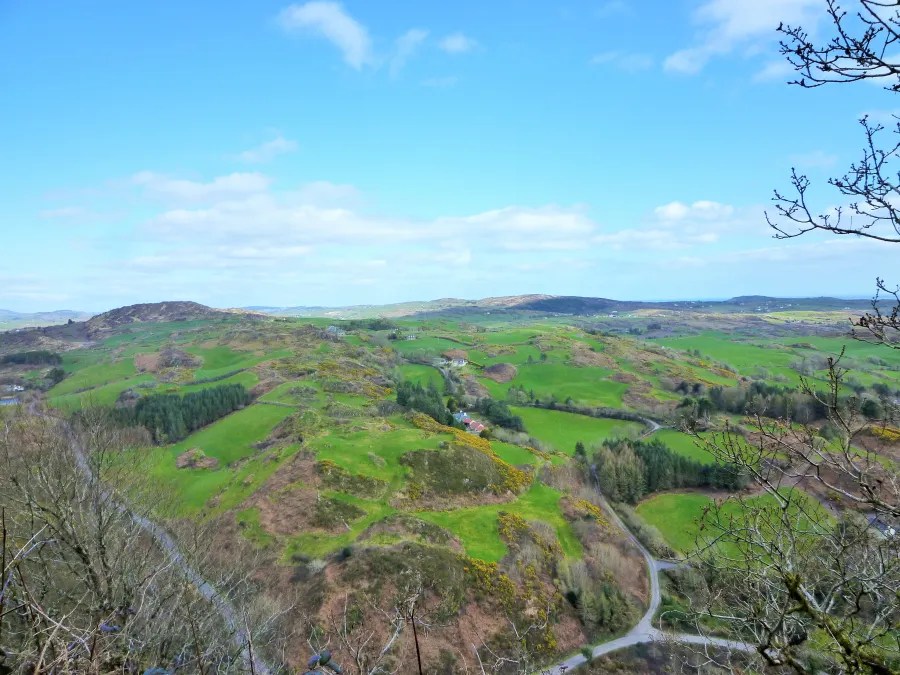 Blick auf eine grüne, hügelige Landschaft in Irland unter einem klaren blauen Himmel.