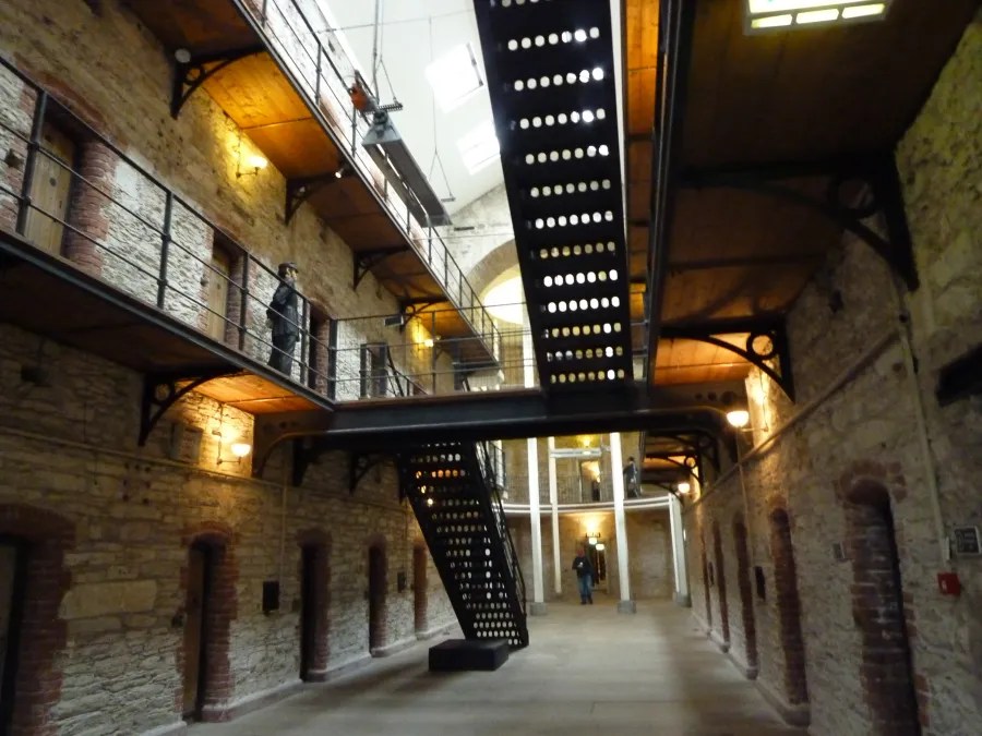 Blick ins Innere eines historischen Gefängnisses mit steinernen Wänden, offenen Galerien und einer modernen Treppe.