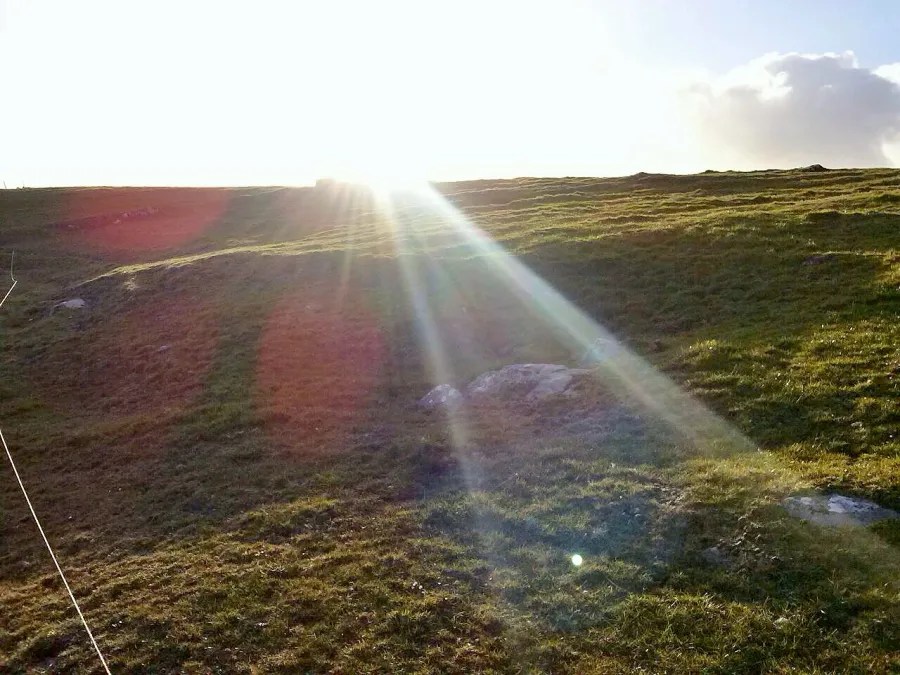 Sonnenstrahlen brechen durch Wolken über einer grünen Wiese, die sanft geschwungene Hügel zeigt.