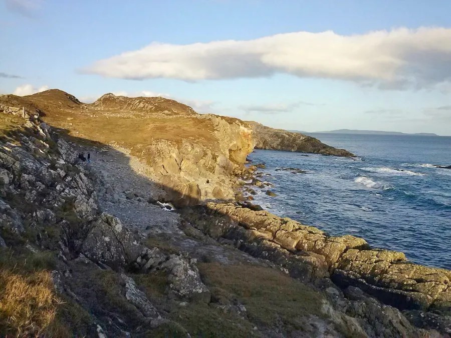 Eine spektakuläre Küstenlinie mit klarem Wasser und einer steinigen Küste unter einem blauen Himmel in Irland.