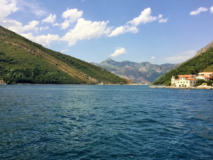 Blick auf das Wasser mit Bergen und Hügeln im Hintergrund, im Vordergrund einige Gebäude am Ufer.