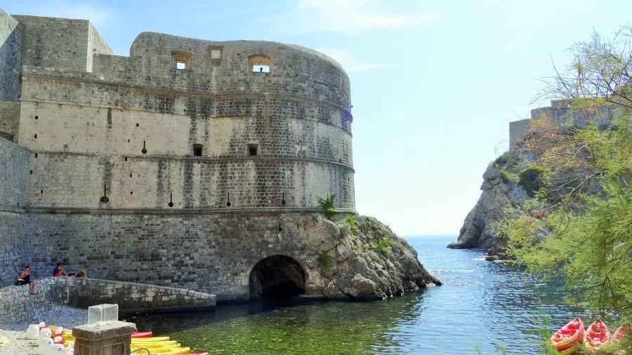 Historisches Steingebäude in Dubrovnik, Kroatien, umgeben von Wasser und Felsen, mit einer mediterranen Landschaft im Hintergrund.