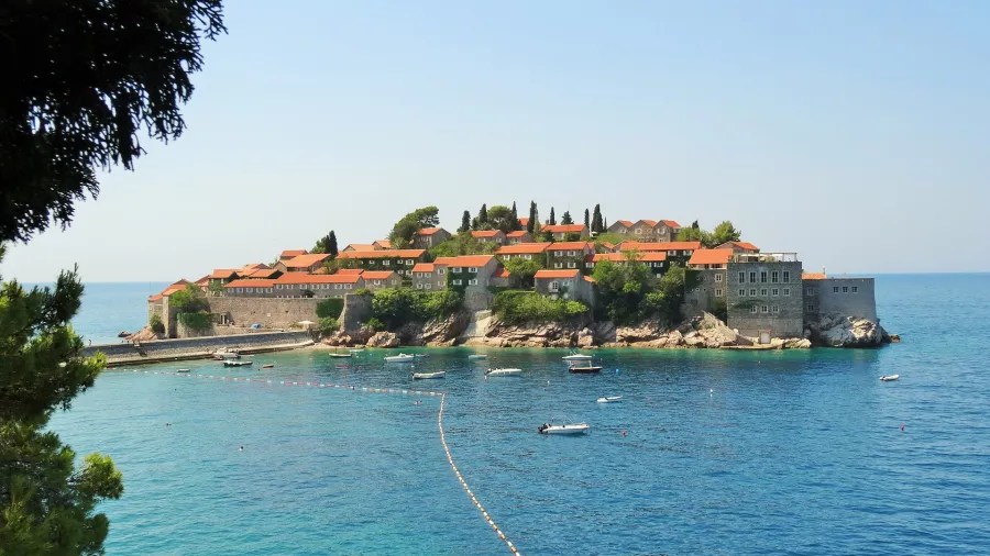 Ein malerischer Blick auf die Insel Sveti Stefan in Montenegro, umgeben von klarem, blauem Wasser und mit einer beeindruckenden, roten Dacharchitektur.