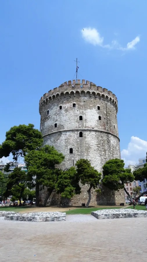 Der Weiße Turm von Thessaloniki, ein historisches Wahrzeichen, umgeben von Bäumen und blauen Himmel.