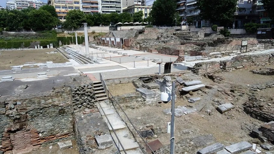 Archäologische Stätte in Thessaloniki mit antiken Ruinen, darunter Säulen und Mauern, umgeben von modernen Gebäuden und Bäumen.