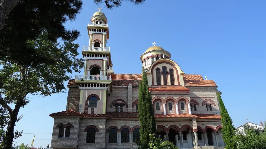 Eine große Kirche mit goldenen Kuppeln und einem rot-weißen Mauerwerk, umgeben von Bäumen und klarem blauem Himmel.