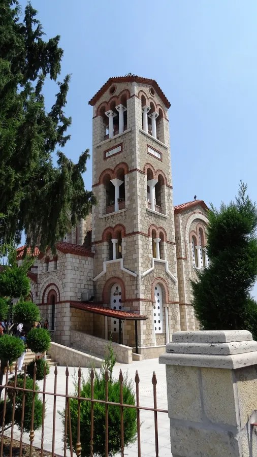 Eine Ansicht einer beeindruckenden Kirche mit einem hohen Glockenturm, umgeben von Bäumen und einem gepflegten Garten.