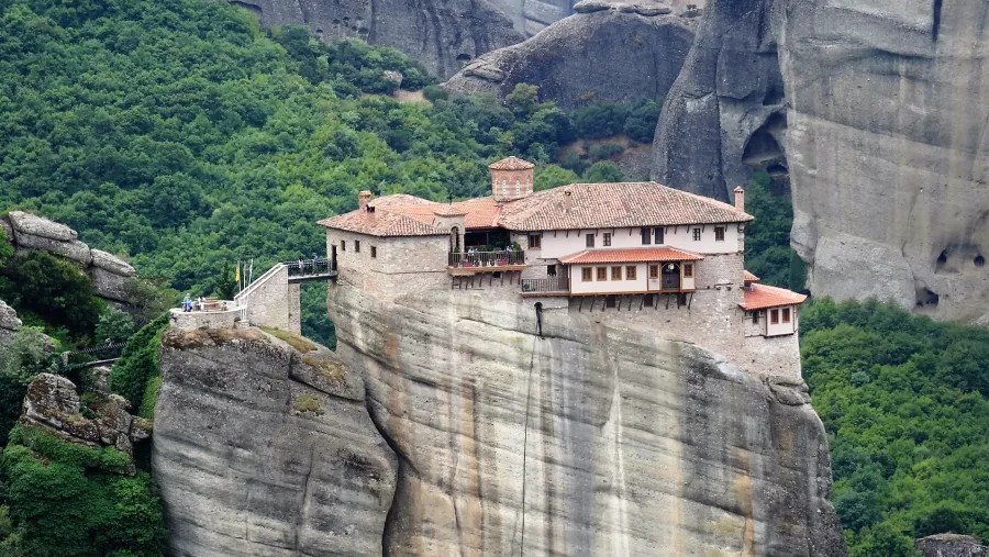 Ein Kloster auf einer steilen Felsnase, umgeben von üppigem Grün und hohen Felsen in Meteora, Griechenland.