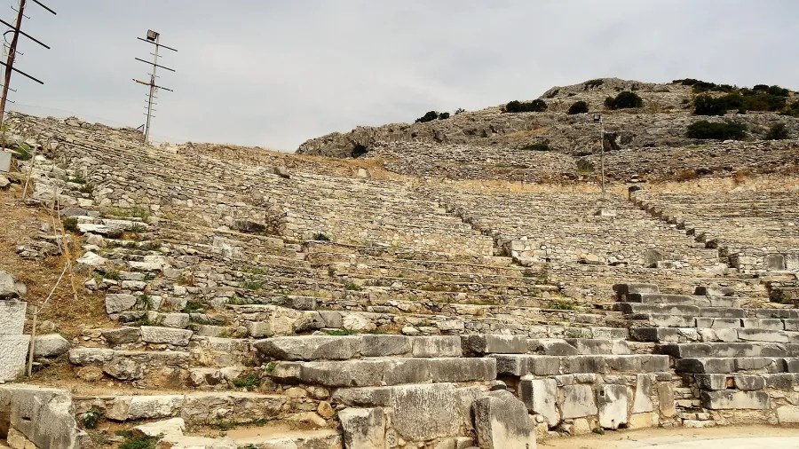 Ruinen eines antiken Amphitheaters, umgeben von trockenen Hügeln und bewölktem Himmel.