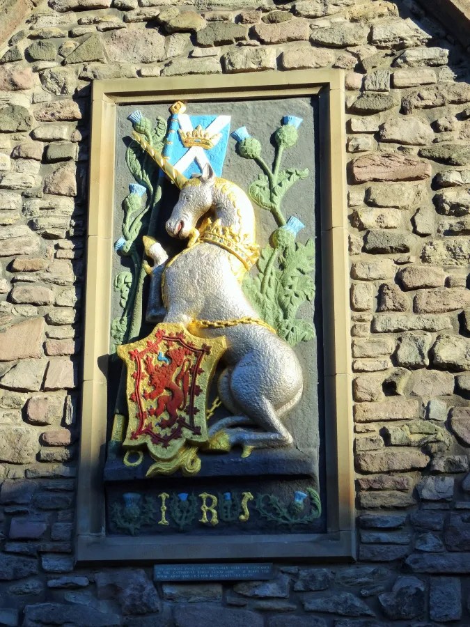Ein Wappen mit einem Einhorn und einem Löwen, umgeben von pflanzlichen Motiven, an einer Steinmauer in Schottland.
