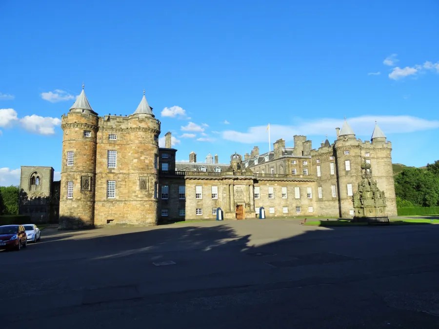 Das Palace of Holyroodhouse, die offizielle Residenz der königlichen Familie in Schottland, dargestellt an einem sonnigen Tag mit blauem Himmel.