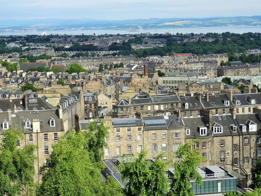 Panorama der Stadt Edinburgh mit grünem Baumbestand und historischen Gebäuden unter blauem Himmel.