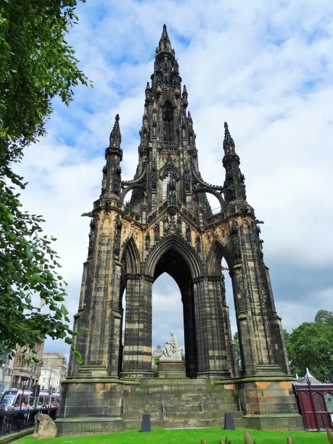 Eine beeindruckende monumentale Struktur mit gotischen Elementen, die in Edinburgh steht. Der Bau ist umgeben von Bäumen und zeigt eine Statue auf einer Treppe, die in der Mitte des Denkmals platziert ist.